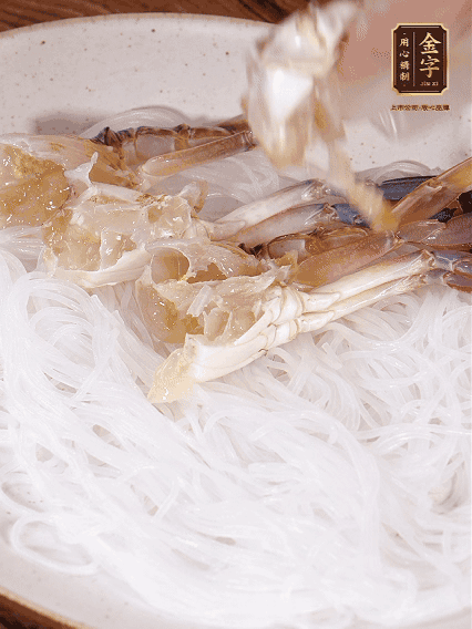 盤底墊上粉絲，擺上梭子蟹、火腿片，撒姜粒，淋上蒸魚豉油、花雕酒調(diào)味腌制15分鐘